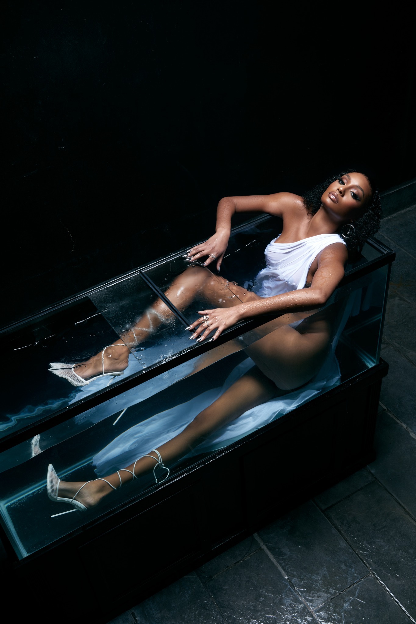 Tiana Parker in a white dress reclining in a glass fish tank